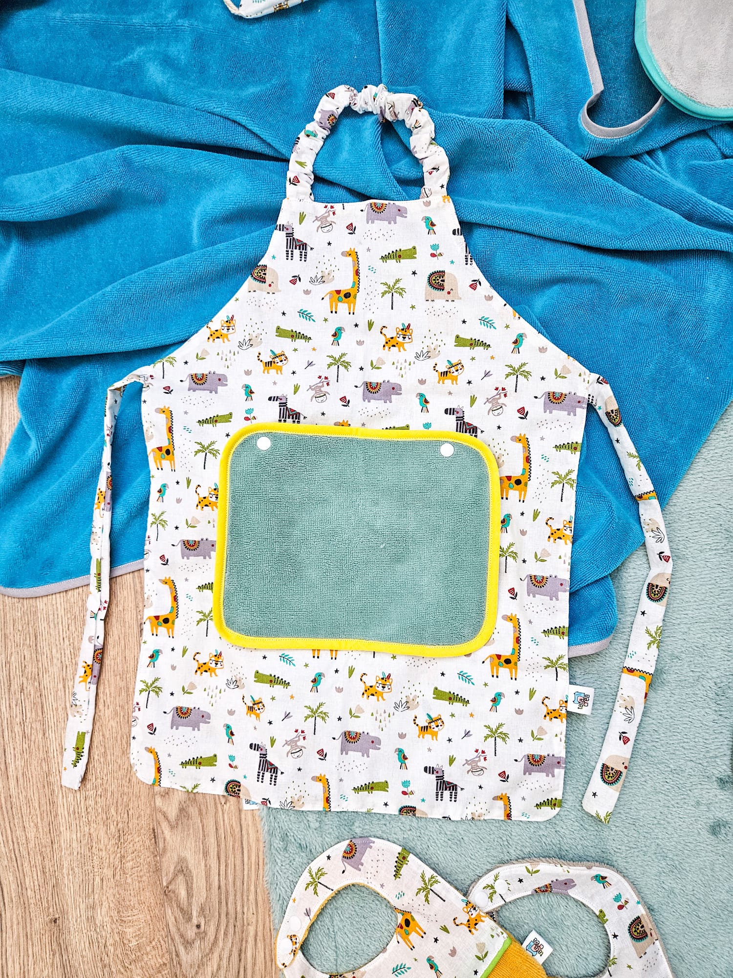 Tablier en attente de personnalisation. Tissu motifs "jungle colorée", avec petite serviette éponge vert tilleul et biais jaune – modèle Tata Créa