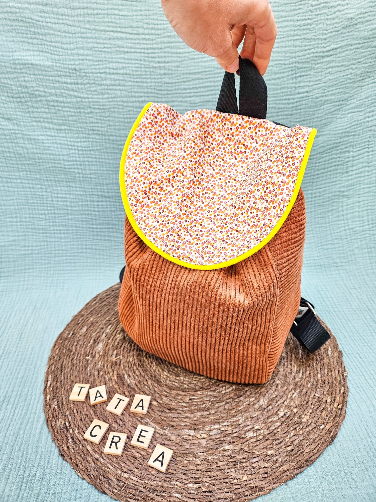 Vue extérieure avant du sac à dos Tata créa - Composé d'un tissu à motifs "fleurs oranges", d'un liseré intermédiaire jaune, d'un velours côtelé marron, et de sangles en coton noires. Les bretelles sont réglables