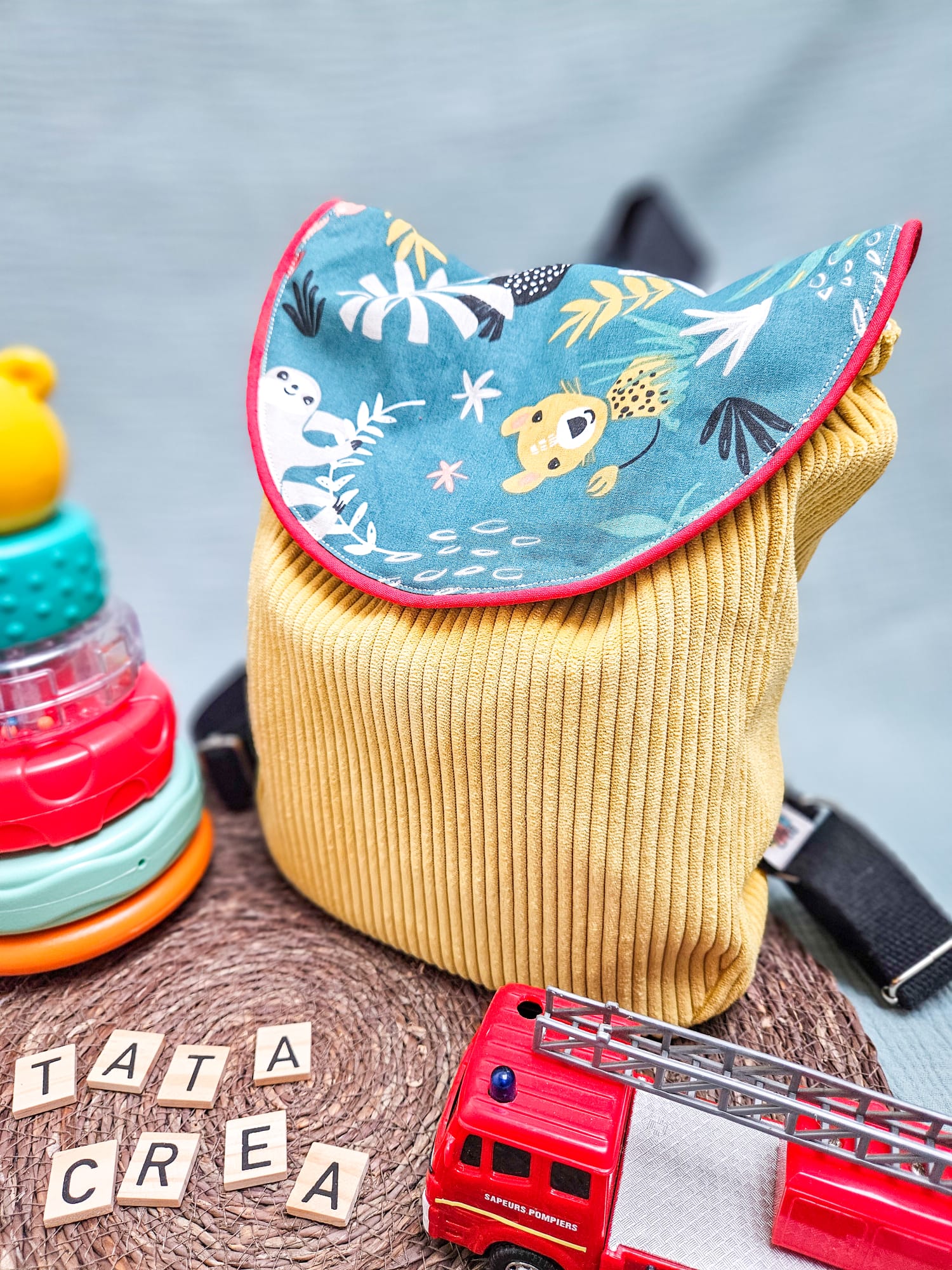 Vue extérieure avant du sac à dos Tata créa - Composé d'un tissu à motifs "singe papaya", d'un liseré intermédiaire rouge, d'un velours côtelé jaune soleil, et de sangles en coton noires. Les bretelles sont réglables