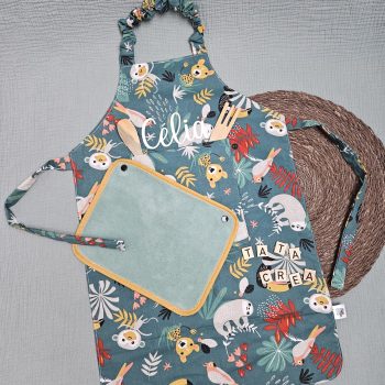 Tablier personnalisé au prénom de Célia, avec ajout d'une poche devant. Tissu motifs "vert singe papaya", avec petite serviette éponge vert tilleul et biais ocre – modèle Tata Créa